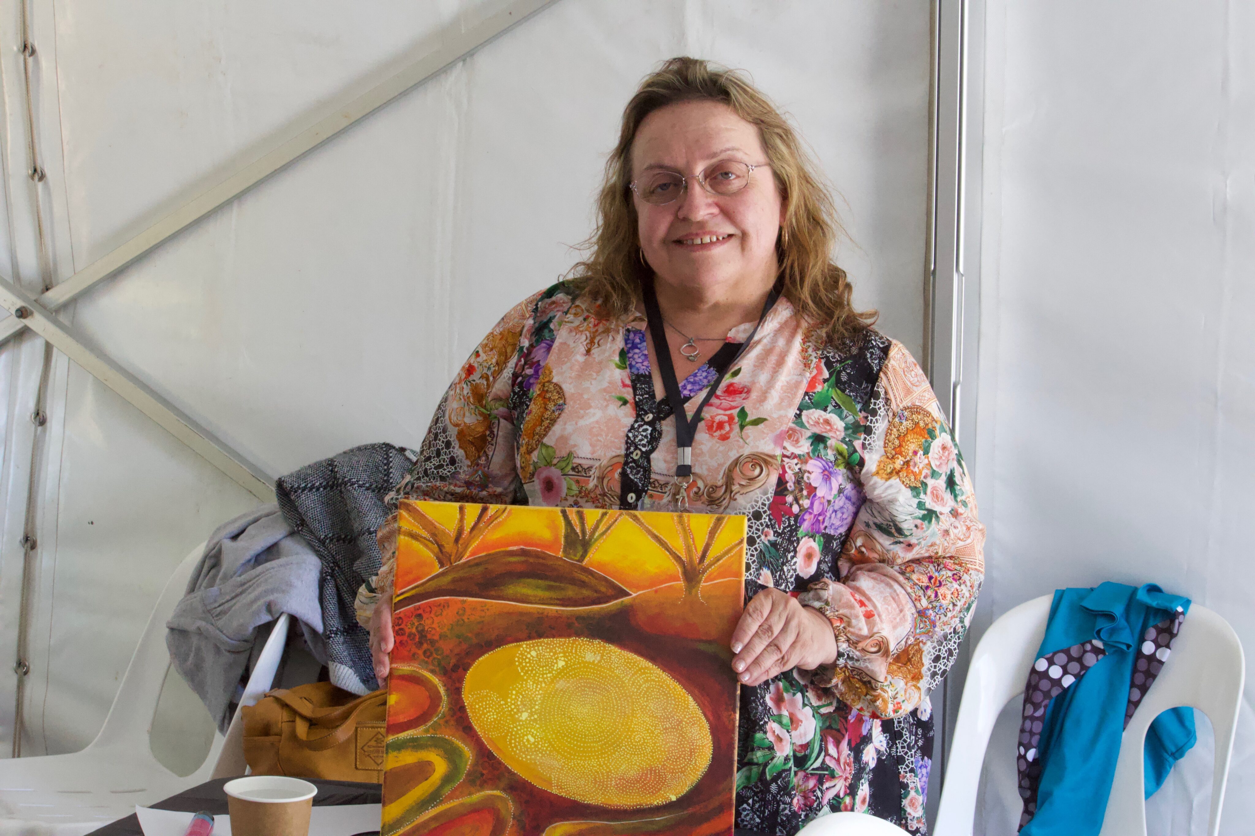An artist and PWdWA member holding up her painting and smiling at the camera.